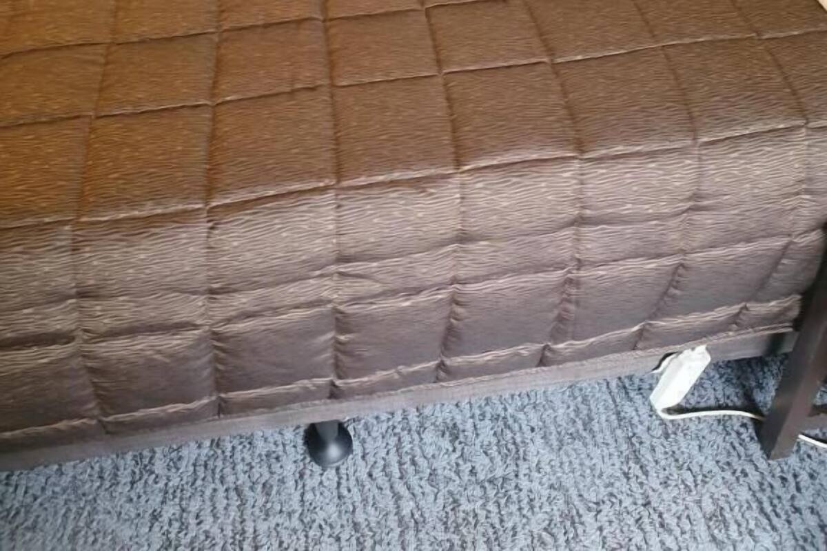 A bed with a brown quilted cover, a white pillow, and a gray carpet.