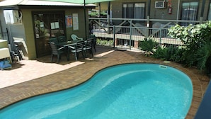 Ein Schwimmbad mit Pflasterdeck und einer kleinen Terrasse mit Stühlen und einem Tisch.