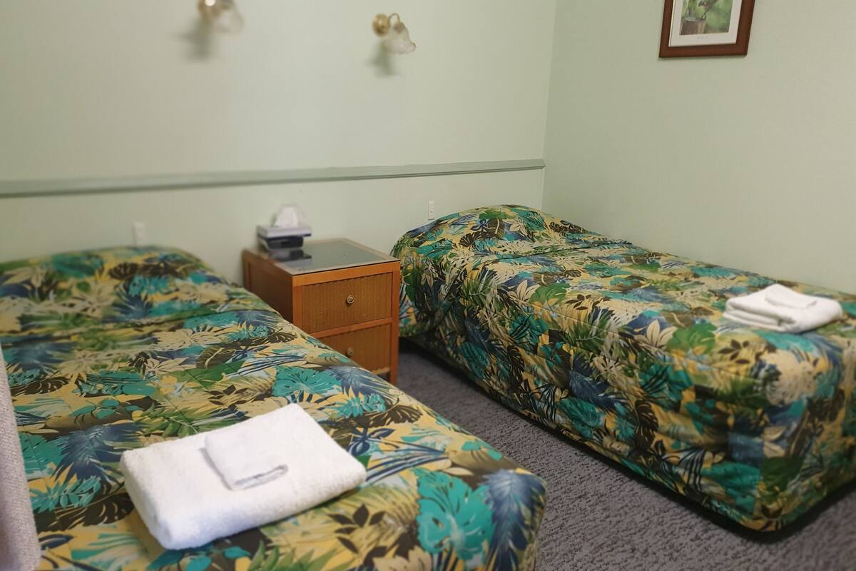 A room with two single beds, a wooden nightstand with a lamp, and a framed picture on the wall.