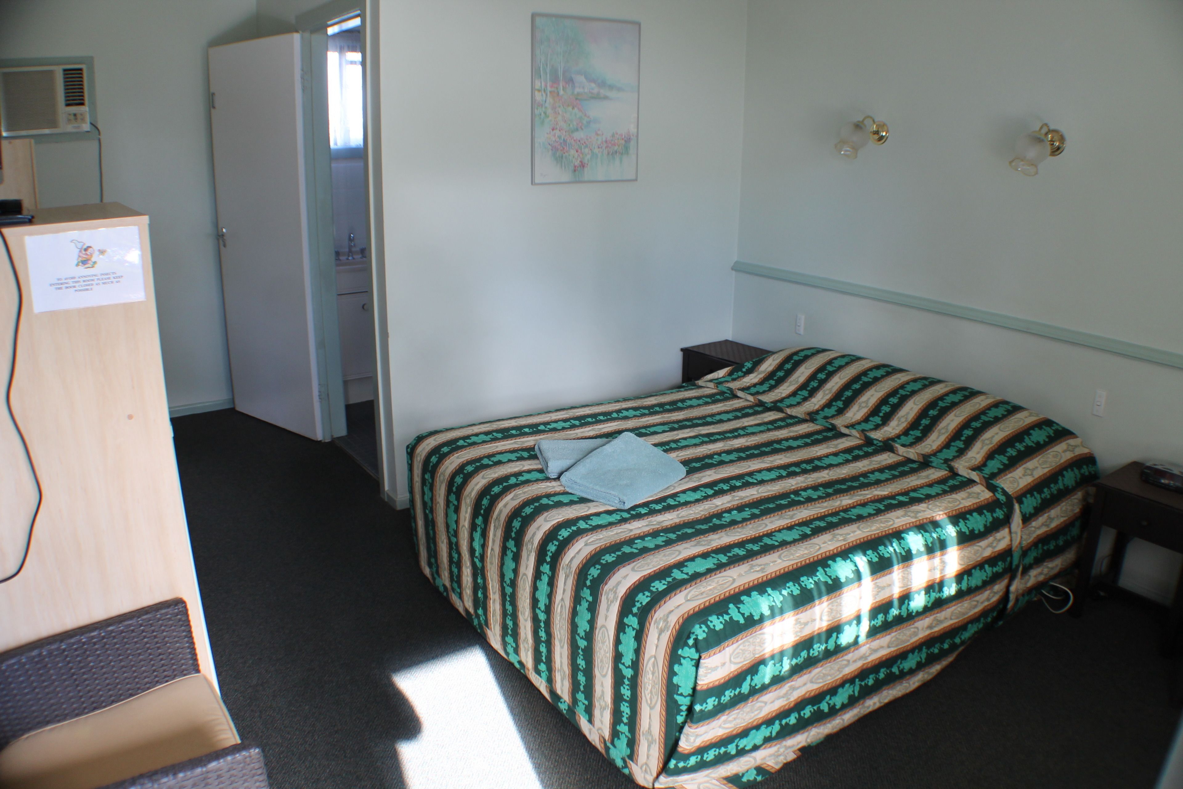 Habitación de hotel con cama, escritorio, silla, armario y un cuadro en la pared.