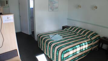 Quarto de hotel com cama, escrivaninha, cadeira, guarda-roupa e um quadro na parede.