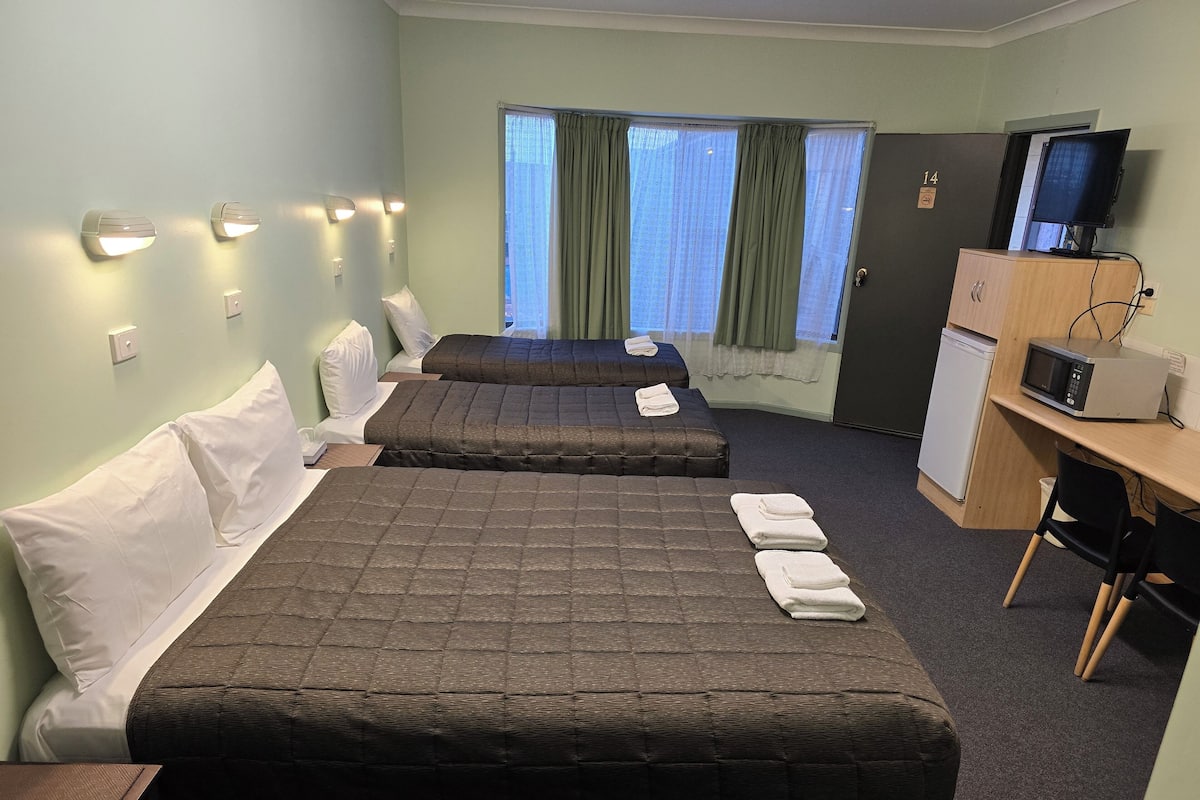 A hotel room with two beds, a desk with a microwave, a TV, and a small refrigerator.