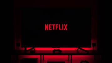 Una habitación oscura con una pantalla iluminada en rojo mostrando el logotipo de Netflix.