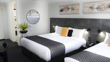 Habitación de hotel con una cama grande, mesitas de noche, una planta en maceta y cuadros en las paredes.