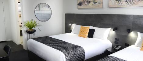 A hotel room with a large bed, bedside tables, a potted plant, and artwork on the walls.