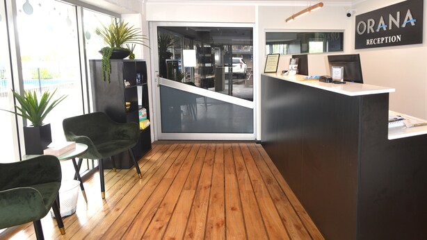 A reception area with a wooden floor, green chairs, a reception desk, and a sign that reads "ORANA RECEPTION". - Orana Motel Dubbo (Dubbo)
