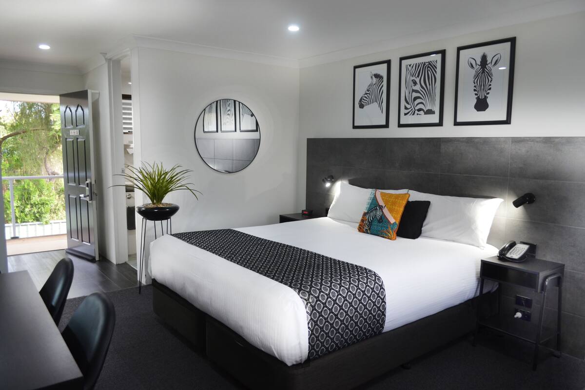 A modern hotel room with a large bed, a bedside table with a phone, a round mirror, and framed artwork on the wall.