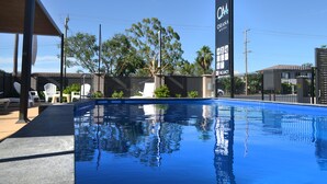 A swimming pool with lounge chairs and a sign for the OM Coruna Motel. - Orana Motel Dubbo (Dubbo)