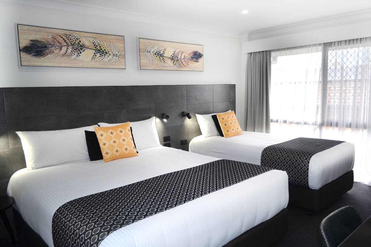 A hotel room with two beds, a dark headboard, and artwork on the wall.