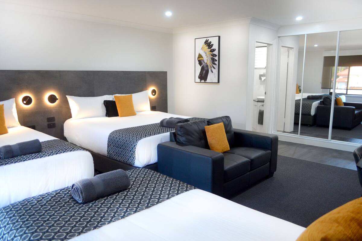 A hotel room with two beds, a sofa, and a large mirror.