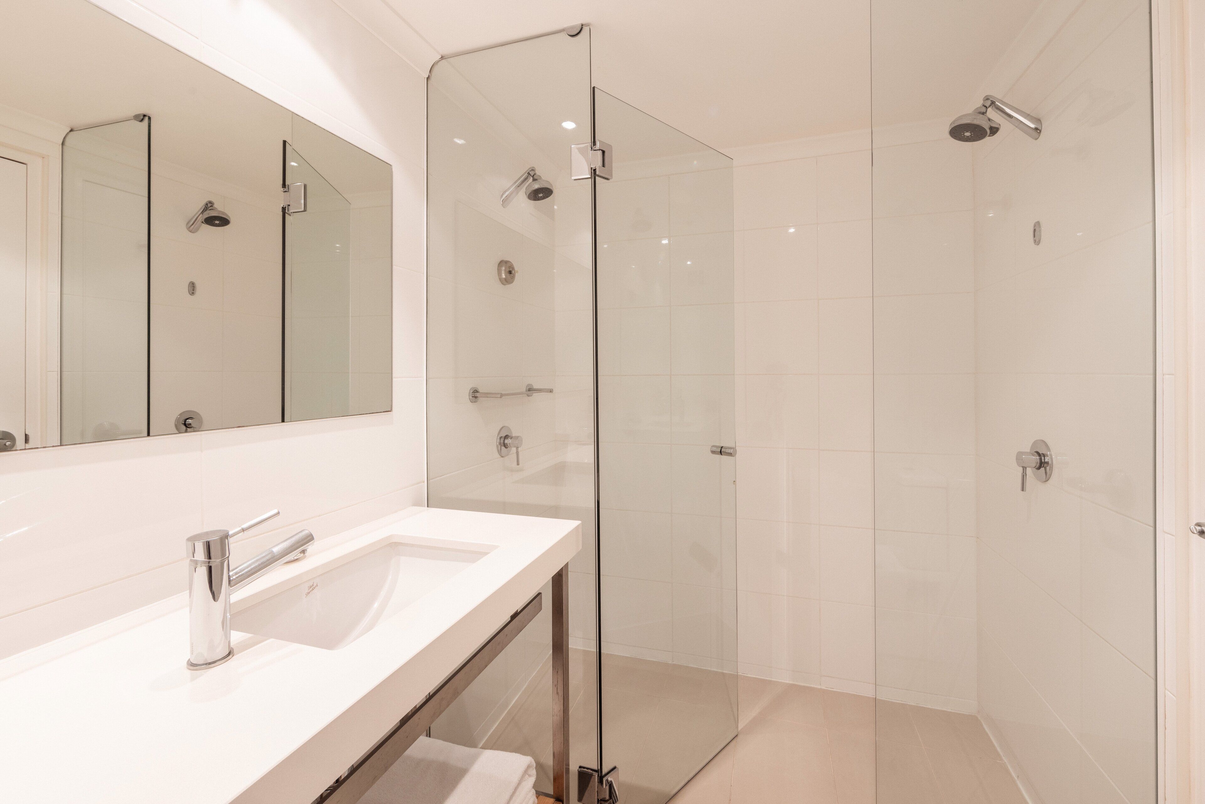 A modern bathroom with a glass-enclosed shower, a white sink, and a large mirror.