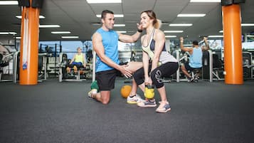 A gym with exercise equipment, a man and a woman performing a stretching exercise, and orange pillars.