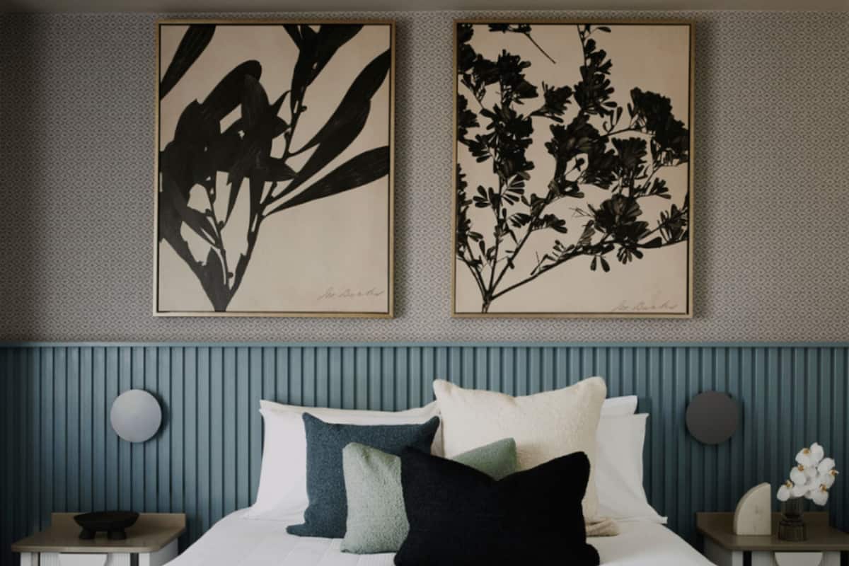 A bedroom with a bed, pillows, a bedside table, and two framed botanical prints on the wall.