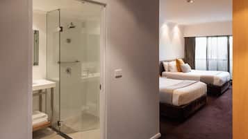 A modern hotel room with a glass-enclosed shower, a double bed, and a separate bed.