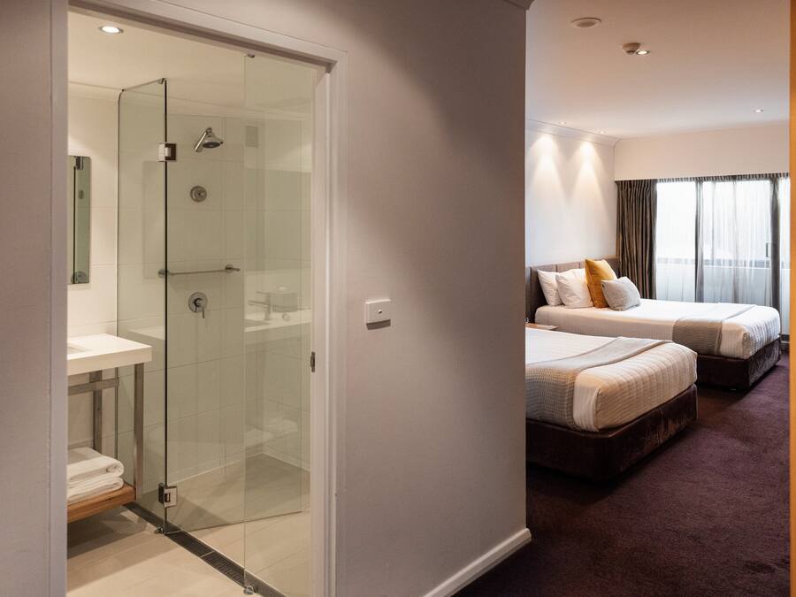 A modern hotel room with a glass-enclosed shower, a double bed, and a separate bed.