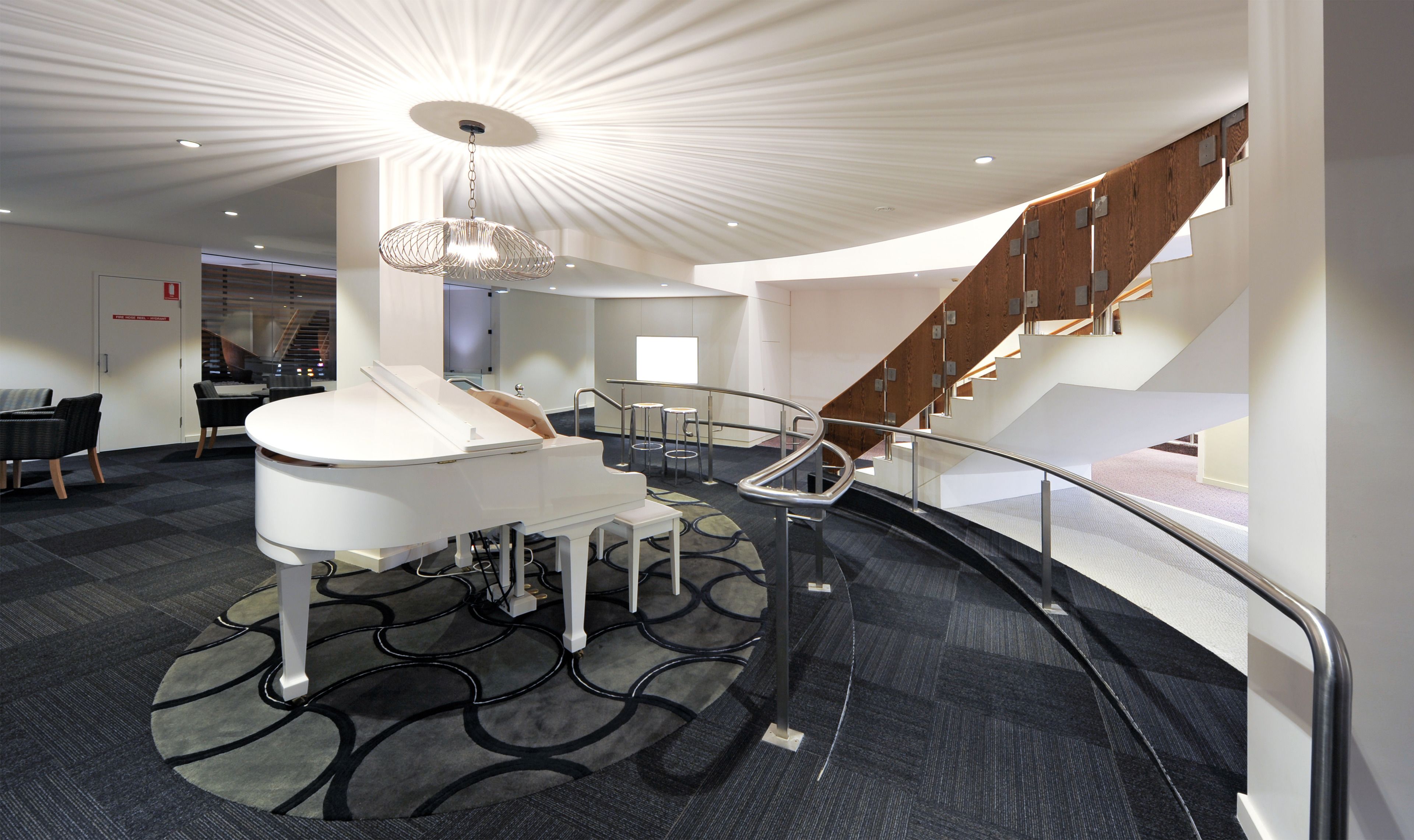 A modern hotel lobby with a piano, a staircase, and a reception desk.