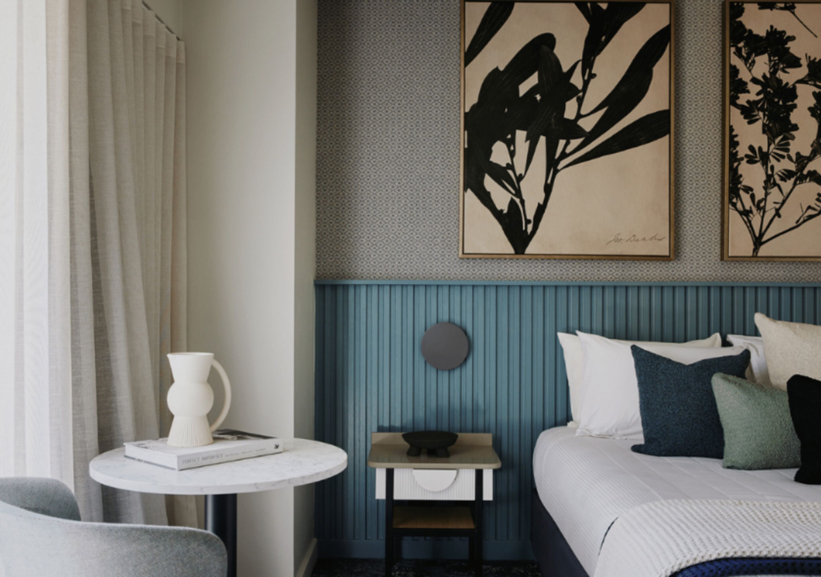 Een hotelkamer met een bed, een nachtkastje met een vaas, een klein bijzettafeltje en twee kunstwerken aan de muur.