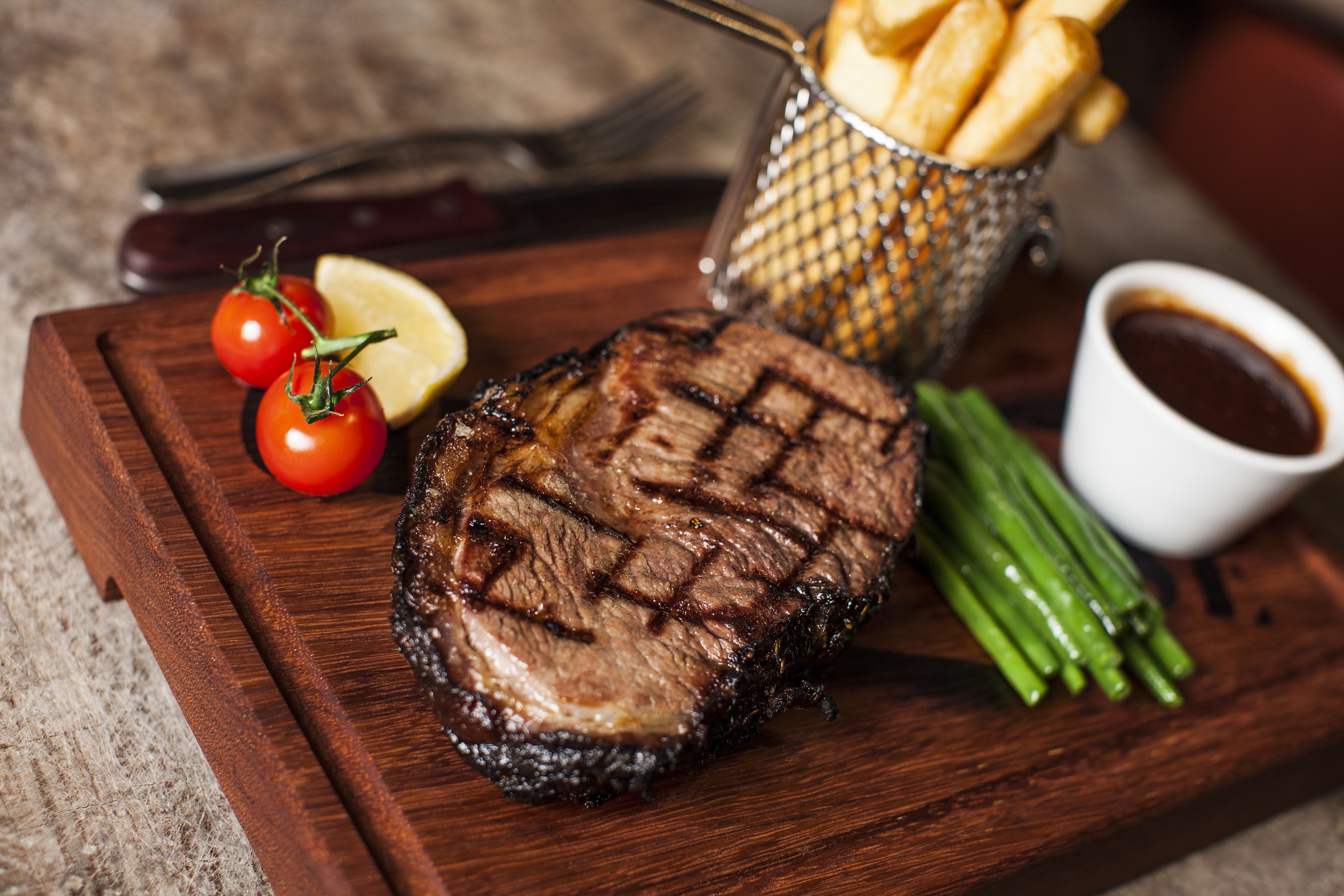 Un plato de carne con papas fritas y vegetales, sobre una tabla de madera.