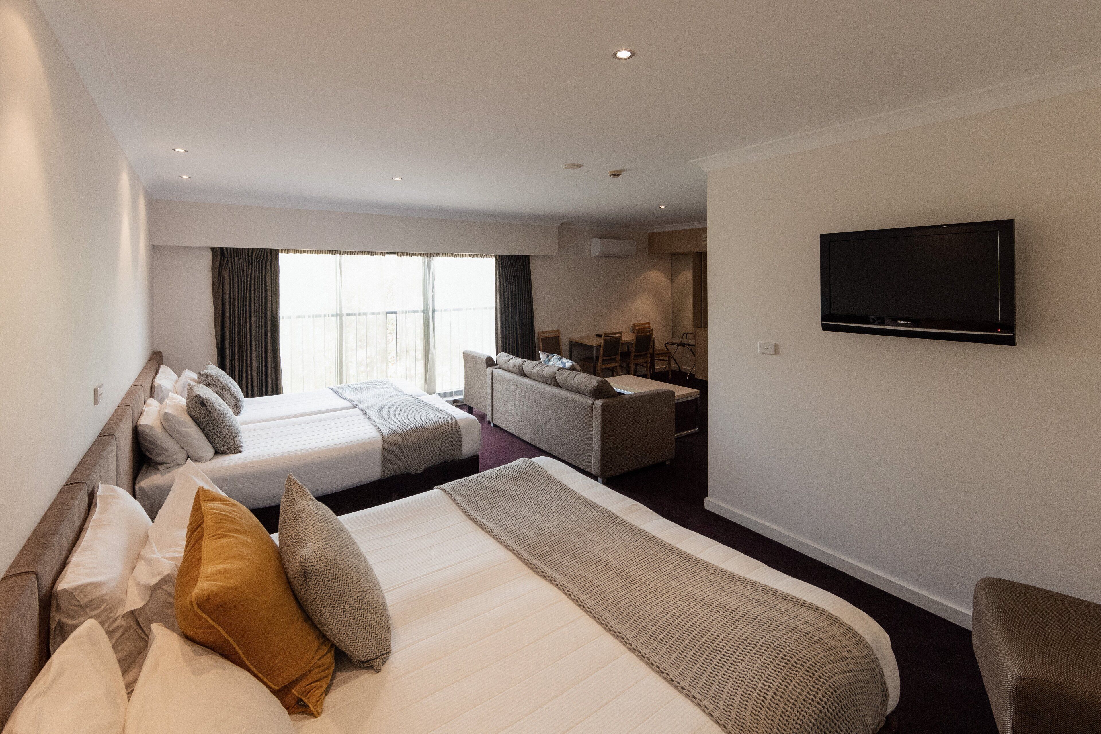 A hotel room with a large bed, two smaller beds, a sofa, a TV, and a dining area.
