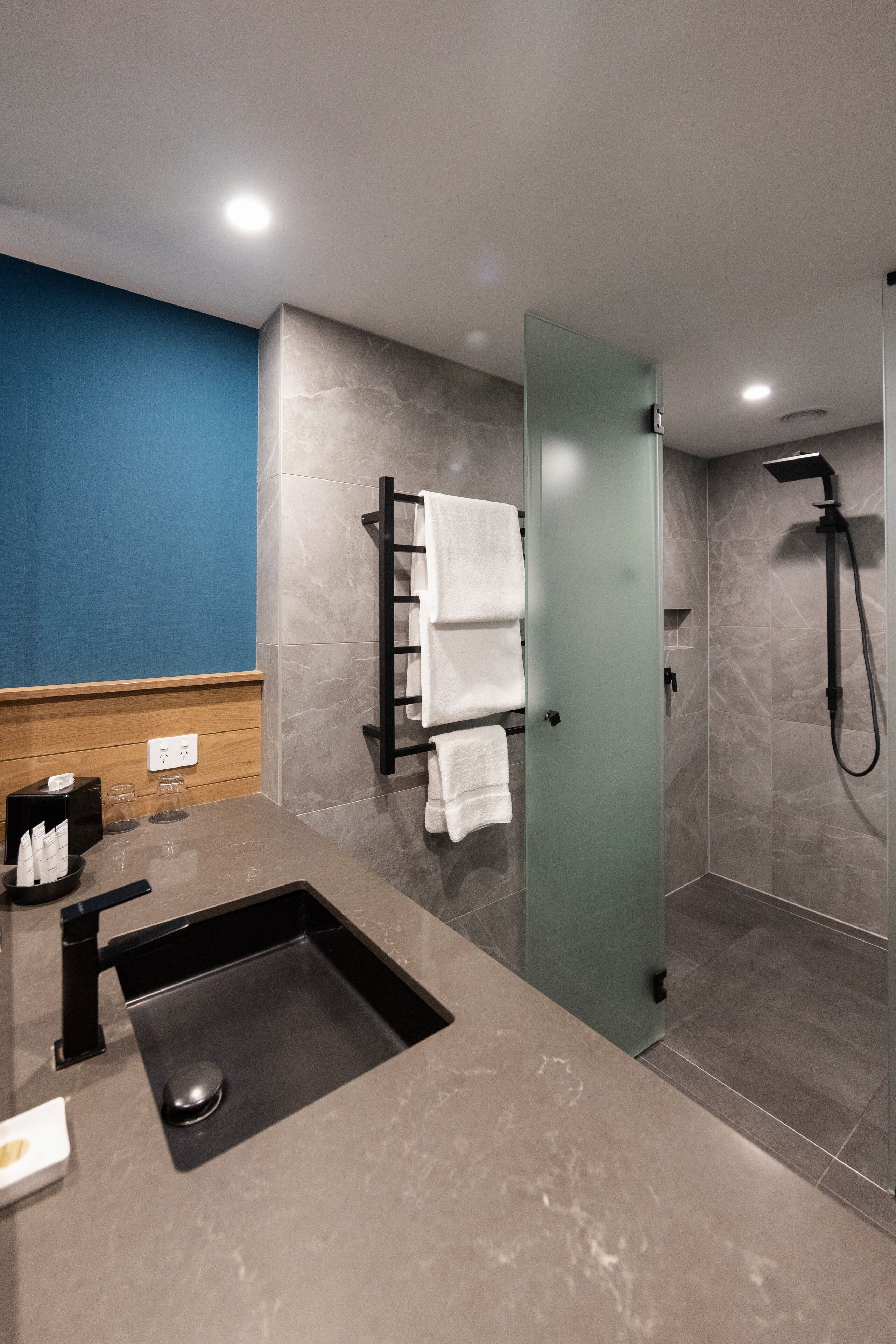 A modern bathroom with a glass shower enclosure, a sink with a black faucet, and a towel rack with white towels.