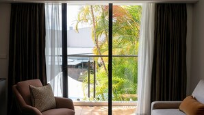 A modern living room with a large sliding glass door leading to a balcony with a view of palm trees. - The Executive Inn (New Lambton)