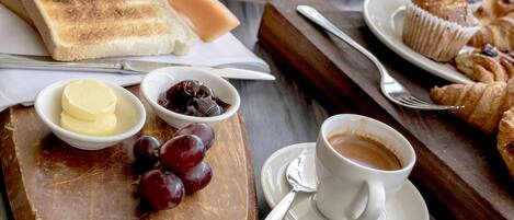 A breakfast setting with toast, butter, jam, croissants, and a cup of coffee on a wooden board.