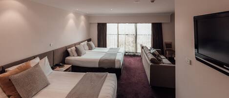 Una habitación de hotel con dos camas, un sofá, un televisor y un ventanal grande.