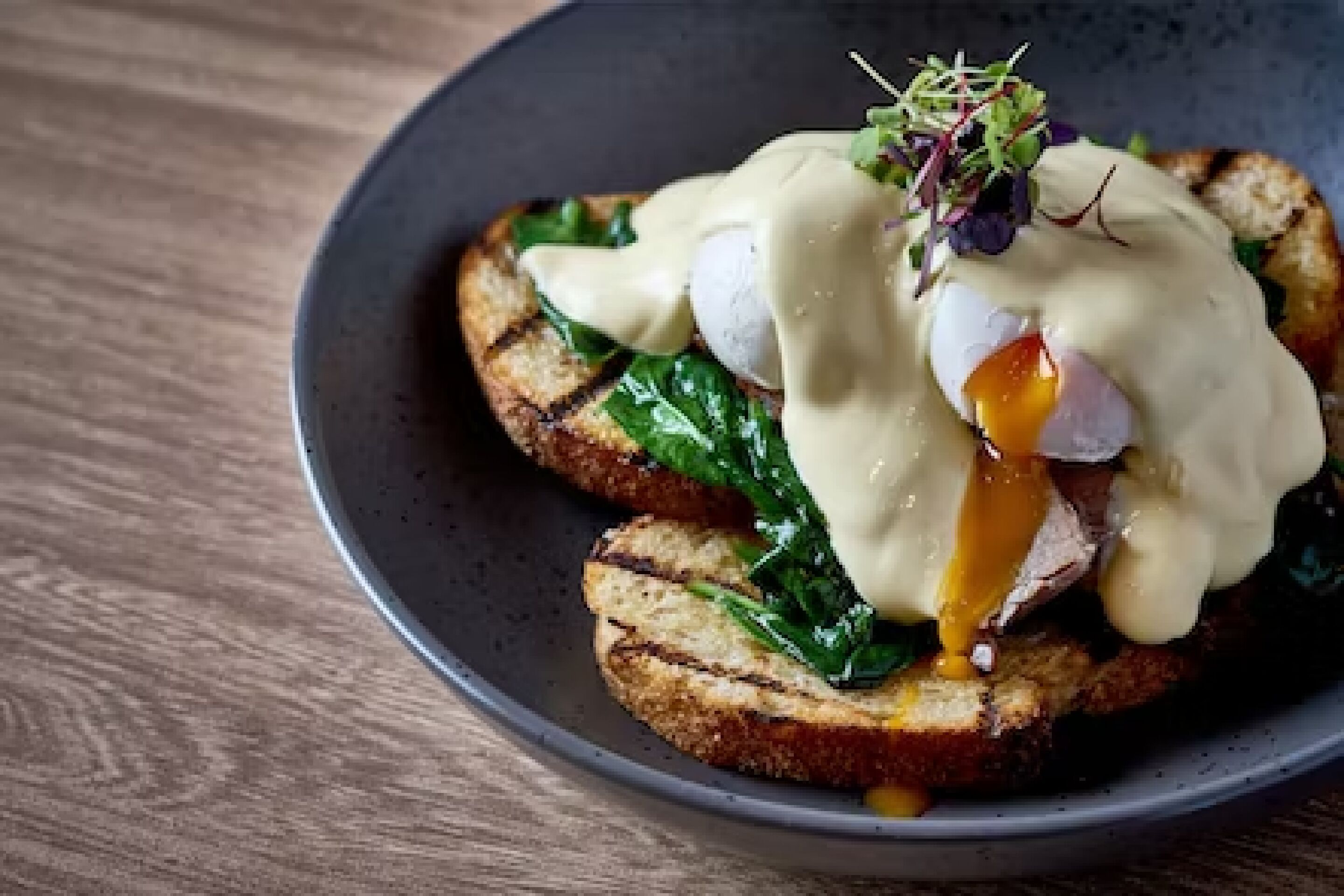 Een bord met een gepocheerd ei, spinazie en hollandaisesaus op toast.