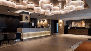 A modern hotel reception area with a central counter, seating area, and a large wall-mounted television. - The Executive Inn (New Lambton)