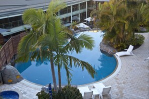 A swimming pool surrounded by palm trees and lounge chairs, with a building in the background.