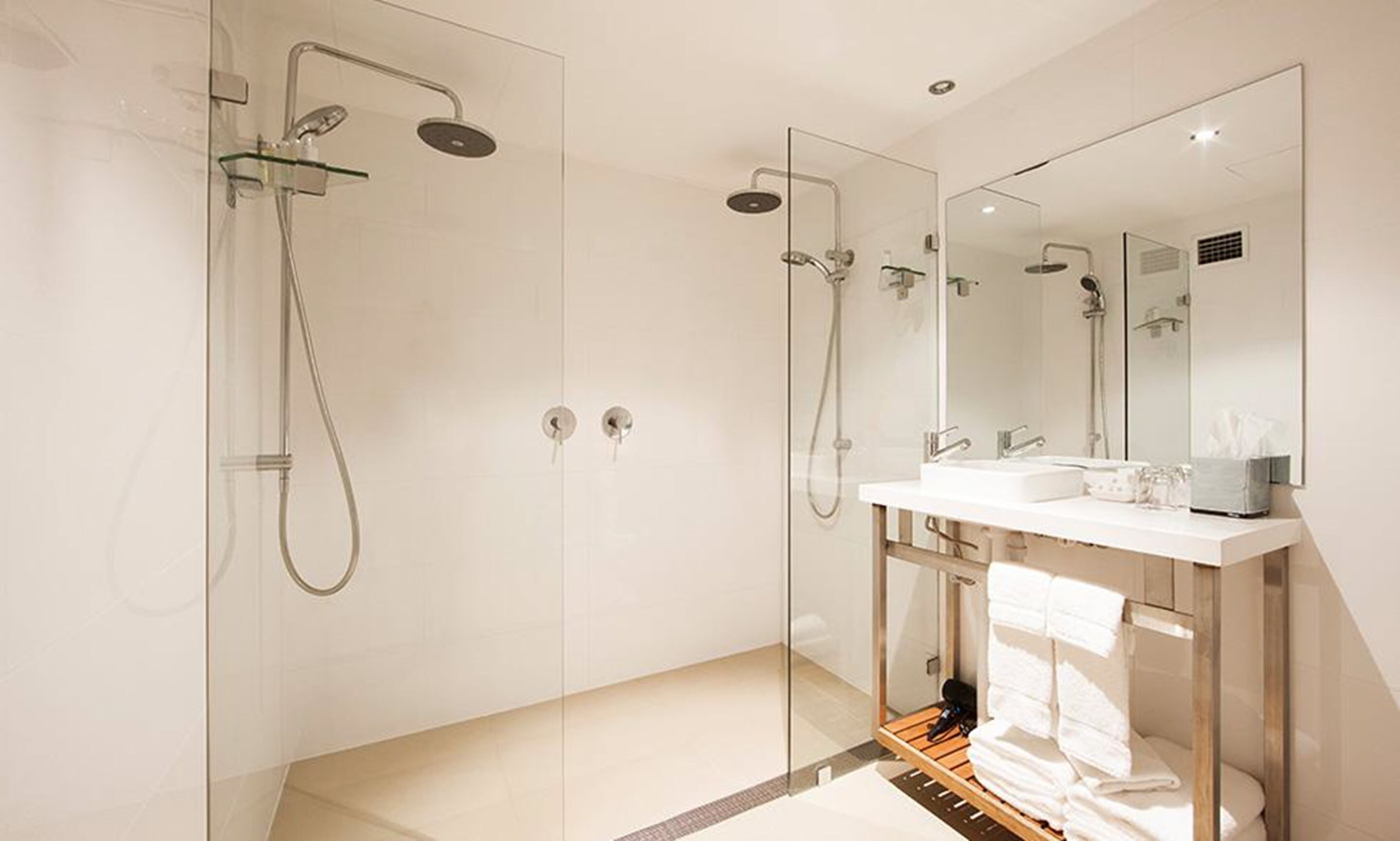 A modern bathroom with a glass-enclosed shower, a white vanity with a mirror, and a towel rack.