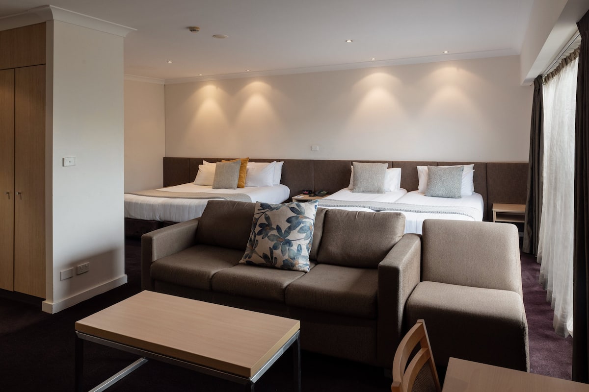 A hotel room with two beds, a sofa, a table, and a wardrobe.