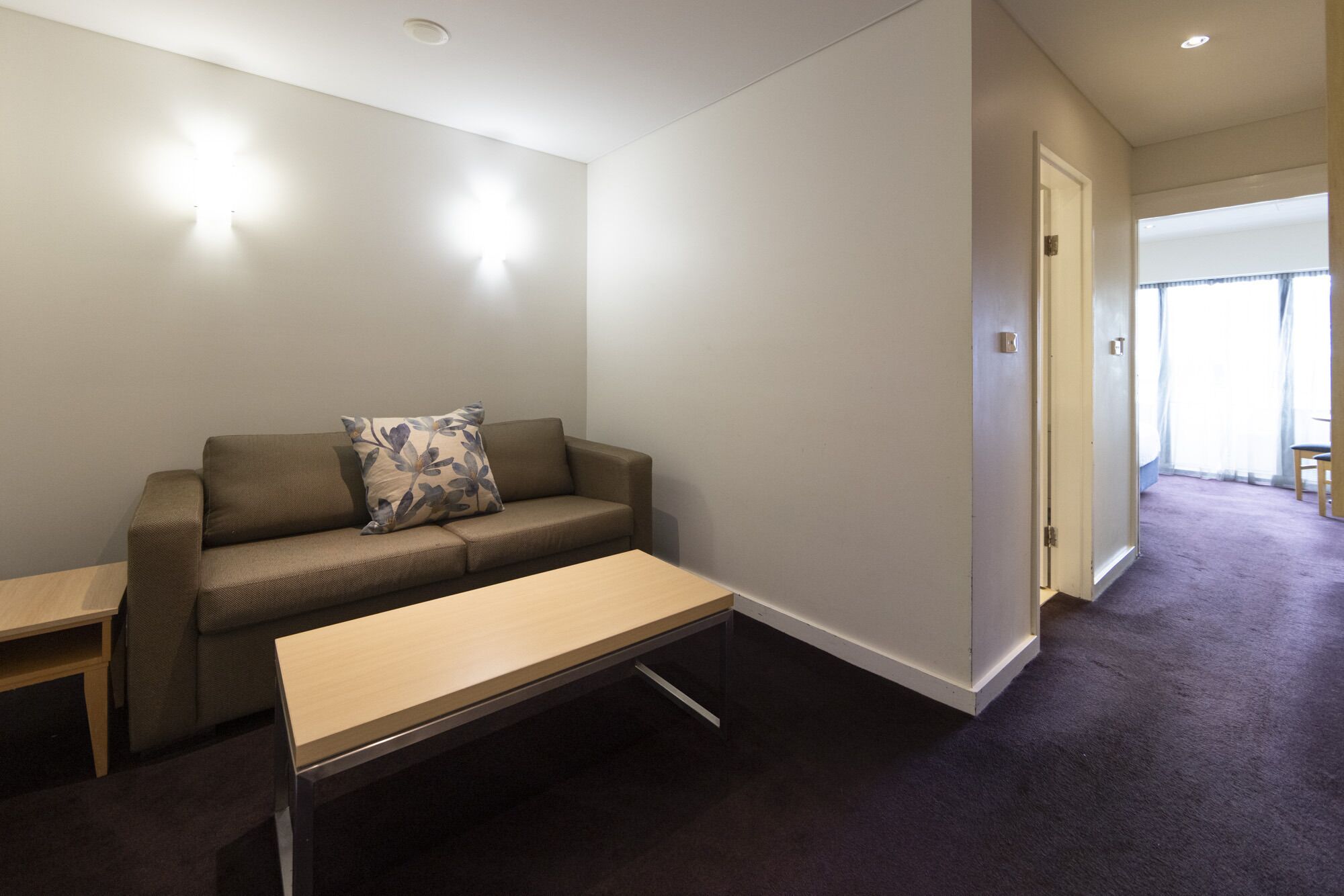 A modern living room with a sofa, a small table, and a door leading to another room.