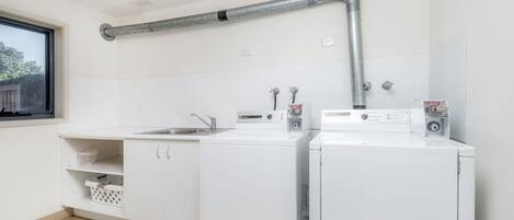 A laundry room with two white washing machines, a sink, and a window.