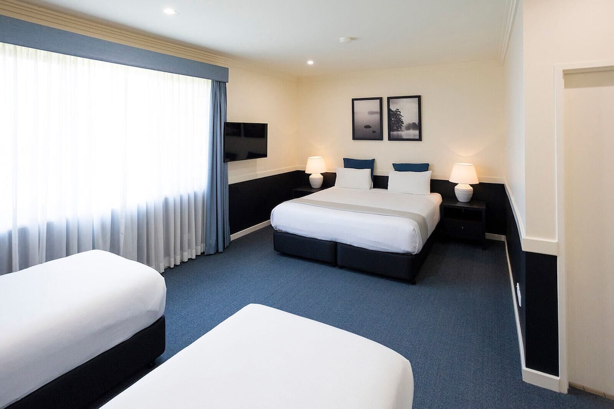 A hotel room with a large bed, two bedside tables with lamps, a flat-screen TV, and a window with curtains.