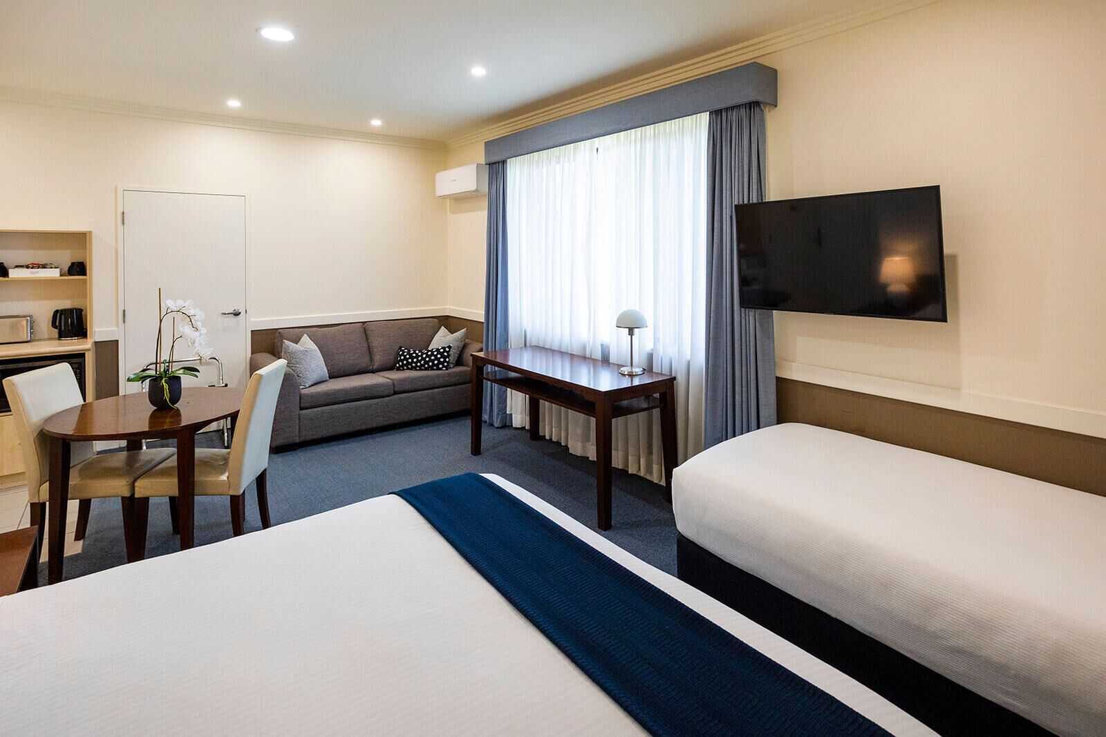 A hotel room with a bed, a sofa, a desk, a TV, and a window with curtains.