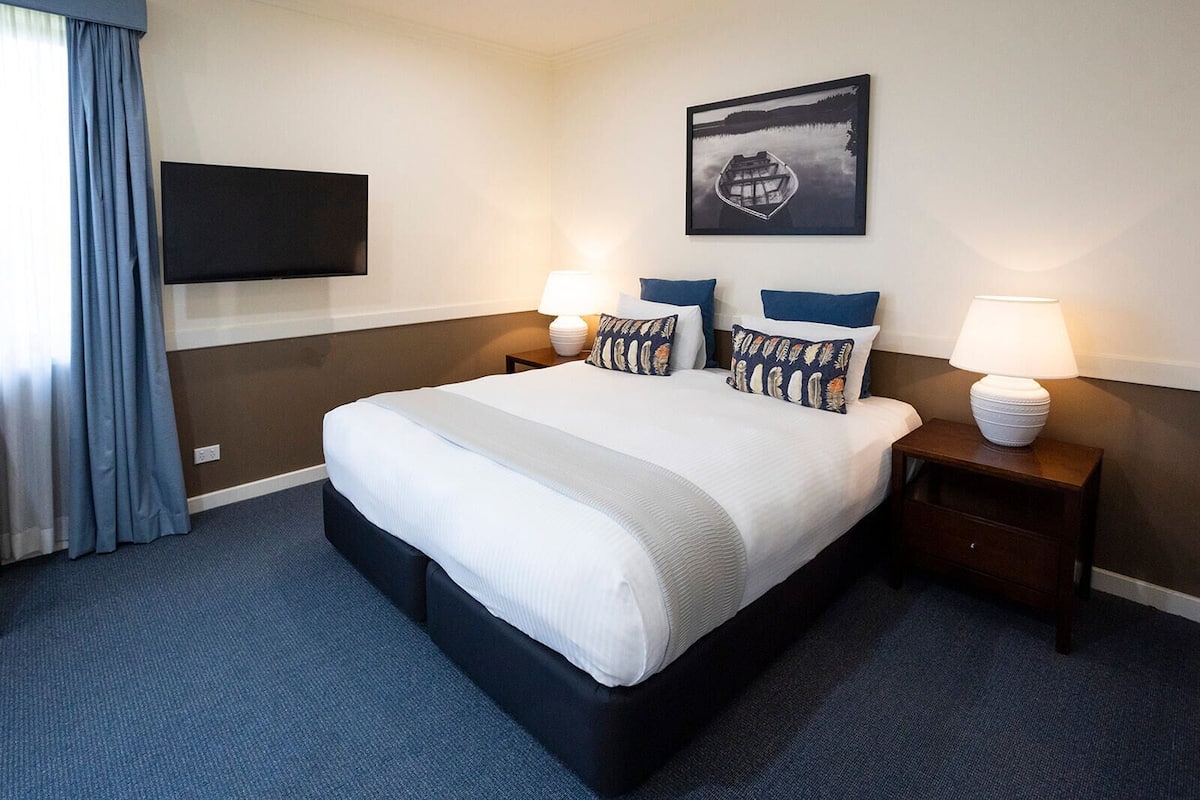 A hotel room with a large bed, two bedside tables with lamps, a flat-screen TV mounted on the wall, and a framed picture above the bed.