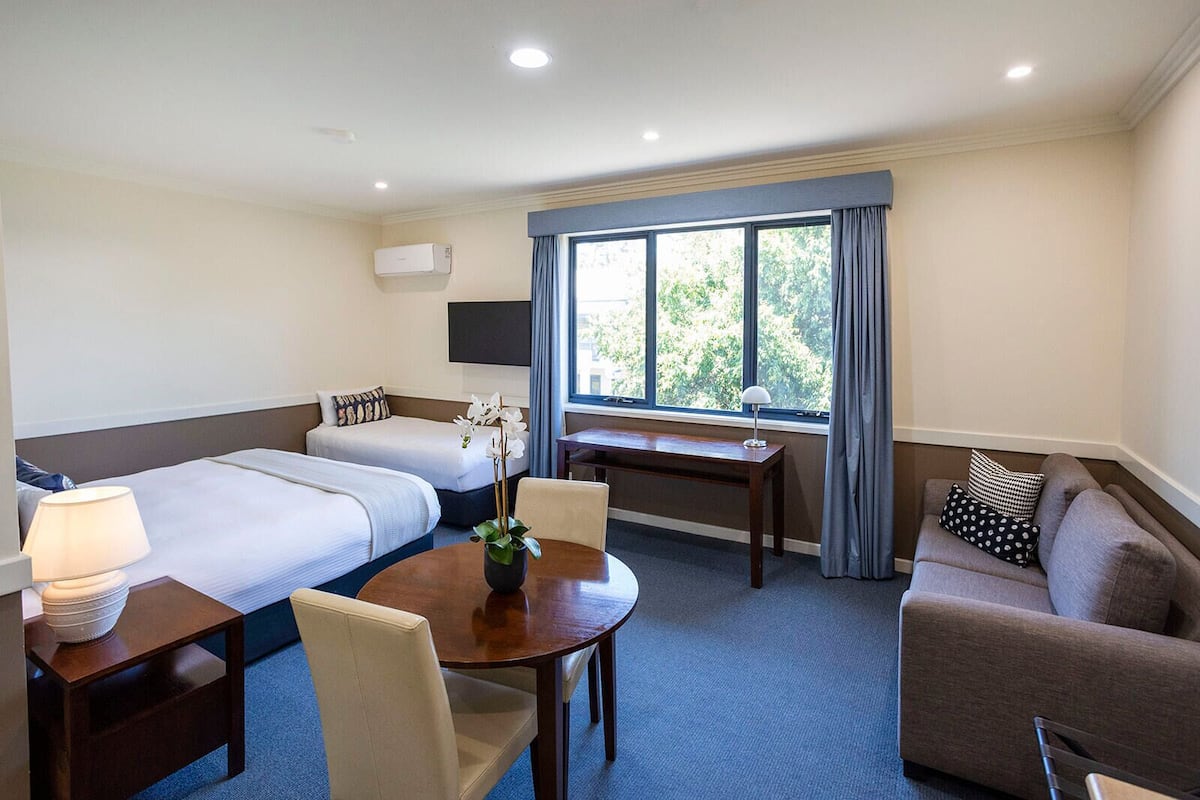 A hotel room with two single beds, a sofa, a dining table, and a TV.