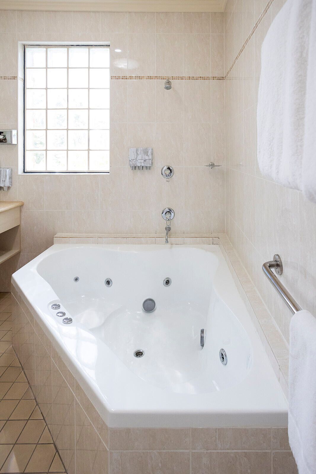 A modern bathroom with a large bathtub, a window, and a towel rack.