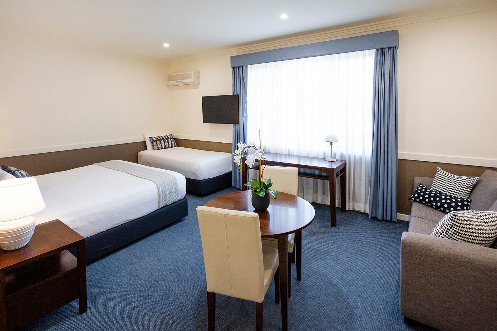 Una habitación de hotel con dos camas individuales, un sofá, una mesa de comedor y un televisor.