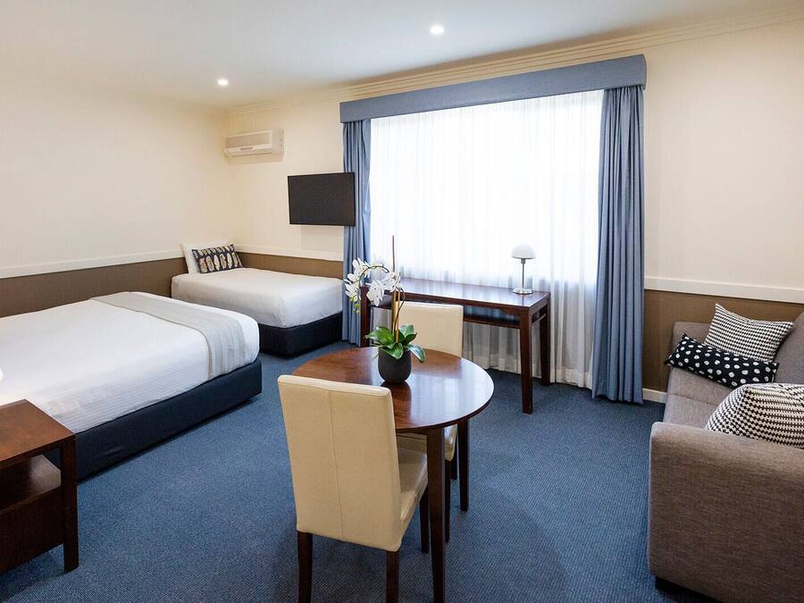 Una habitación de hotel con dos camas individuales, un sofá, una mesa de comedor y un televisor.