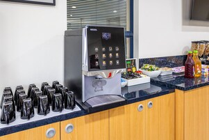 Una estación de café con máquina de Nescafé, vasos desechables, condimentos y refrigerios.