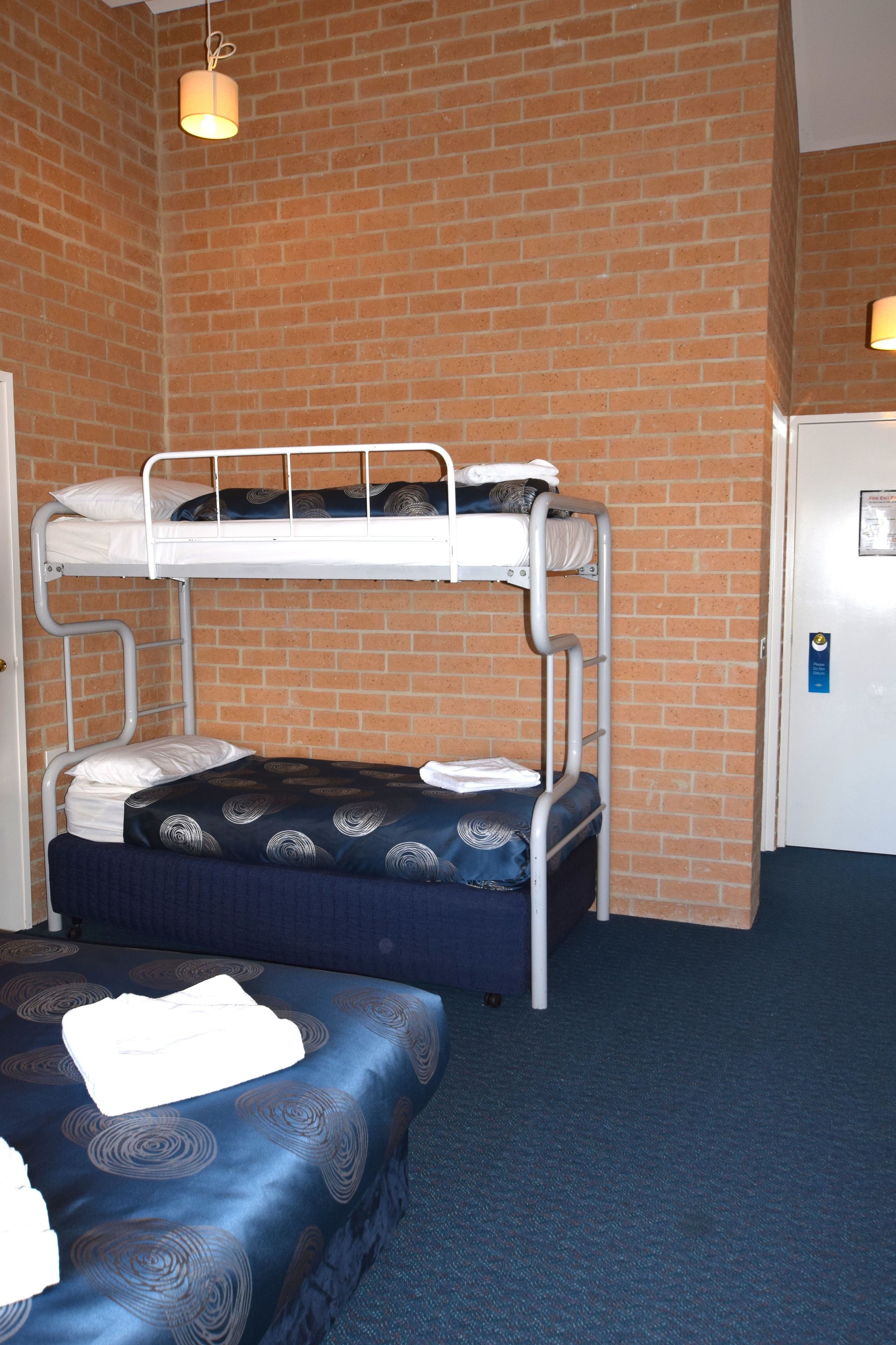Une chambre avec un lit superposé, un mur en briques, une porte et un sol recouvert de moquette.