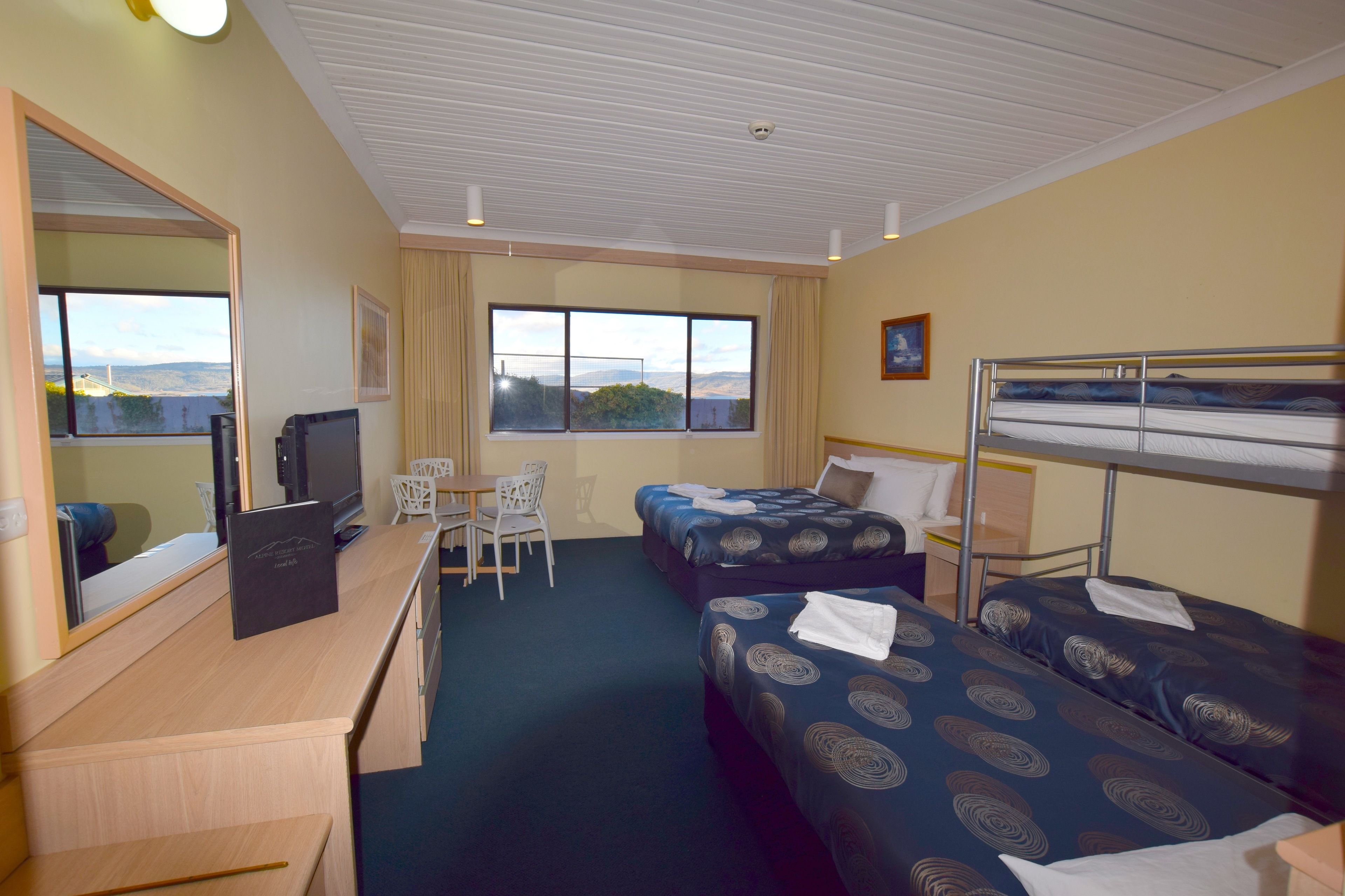 A hotel room with two beds, a desk, a chair, a television, and a window with a view.