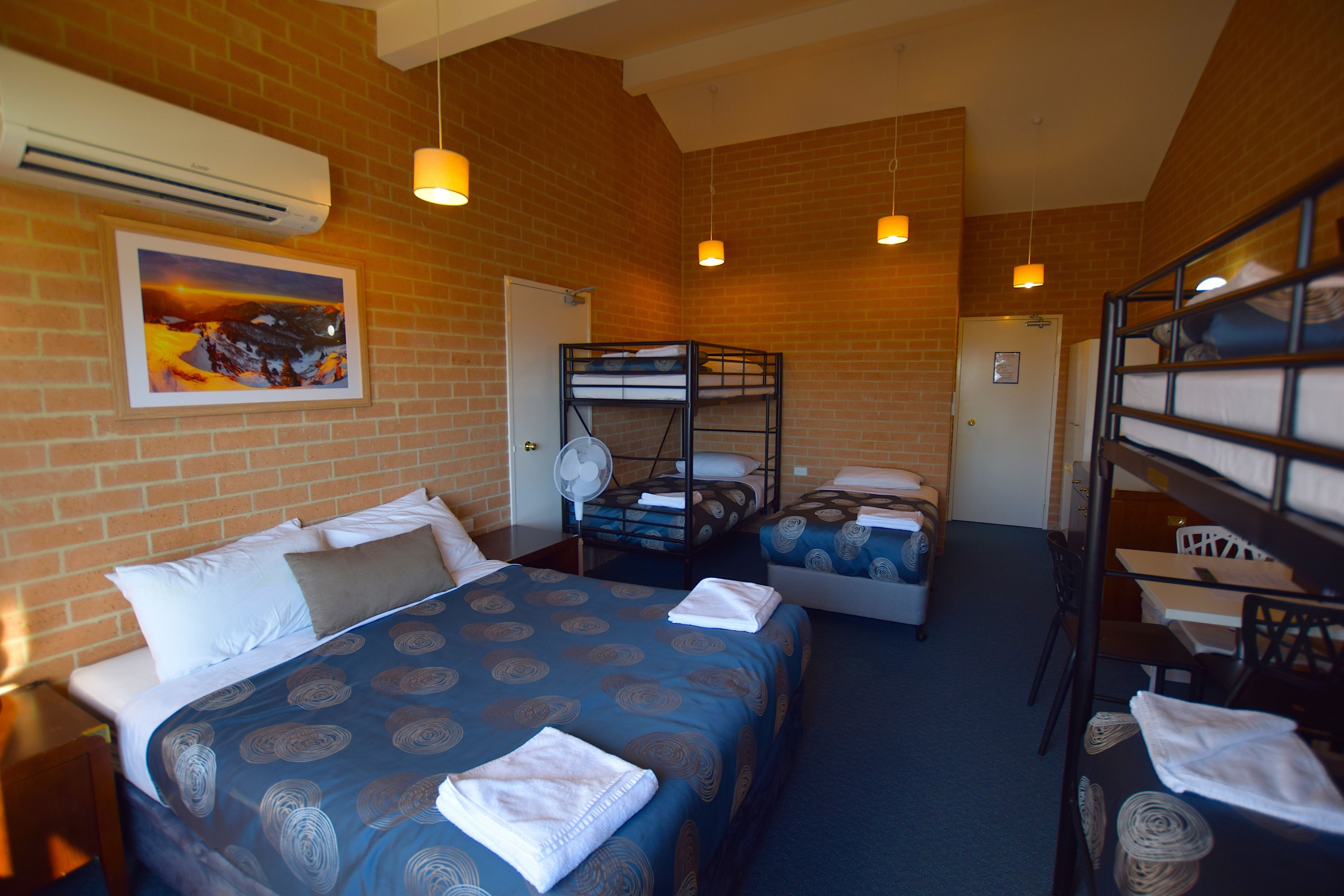 A hotel room with two bunk beds, a desk, and a chair. There is a fan on the wall and a painting on the wall.
