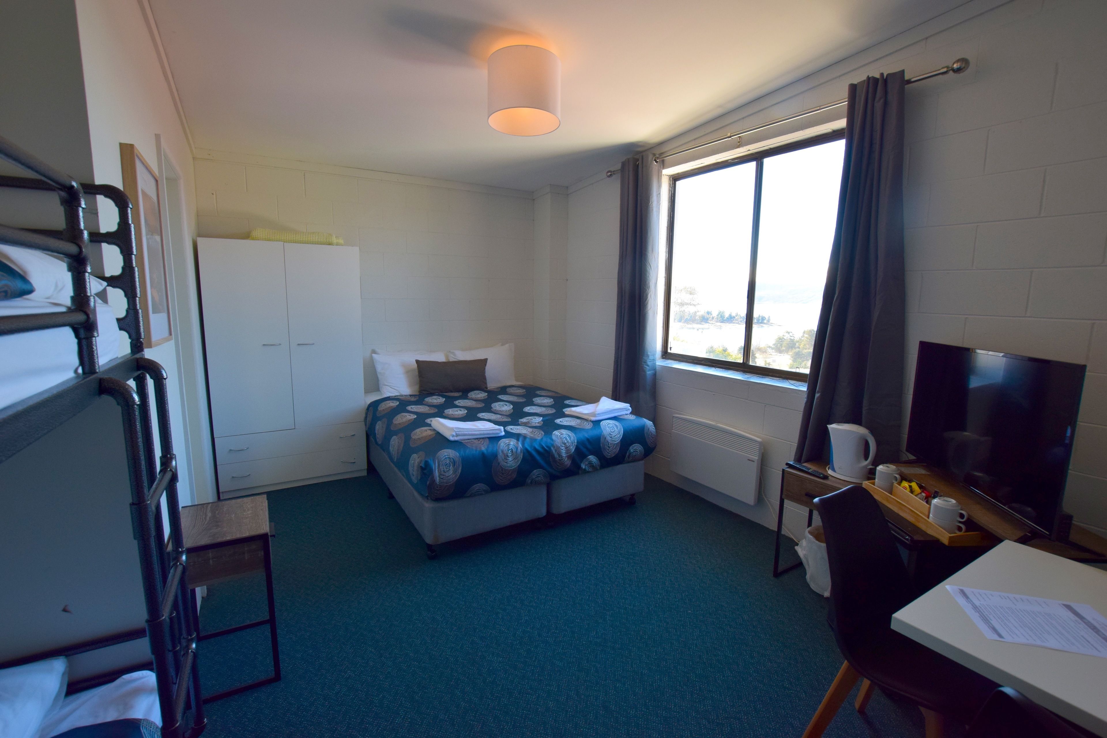 Habitación de hotel con literas, una cama individual, un escritorio con silla, un televisor y una ventana con cortinas.