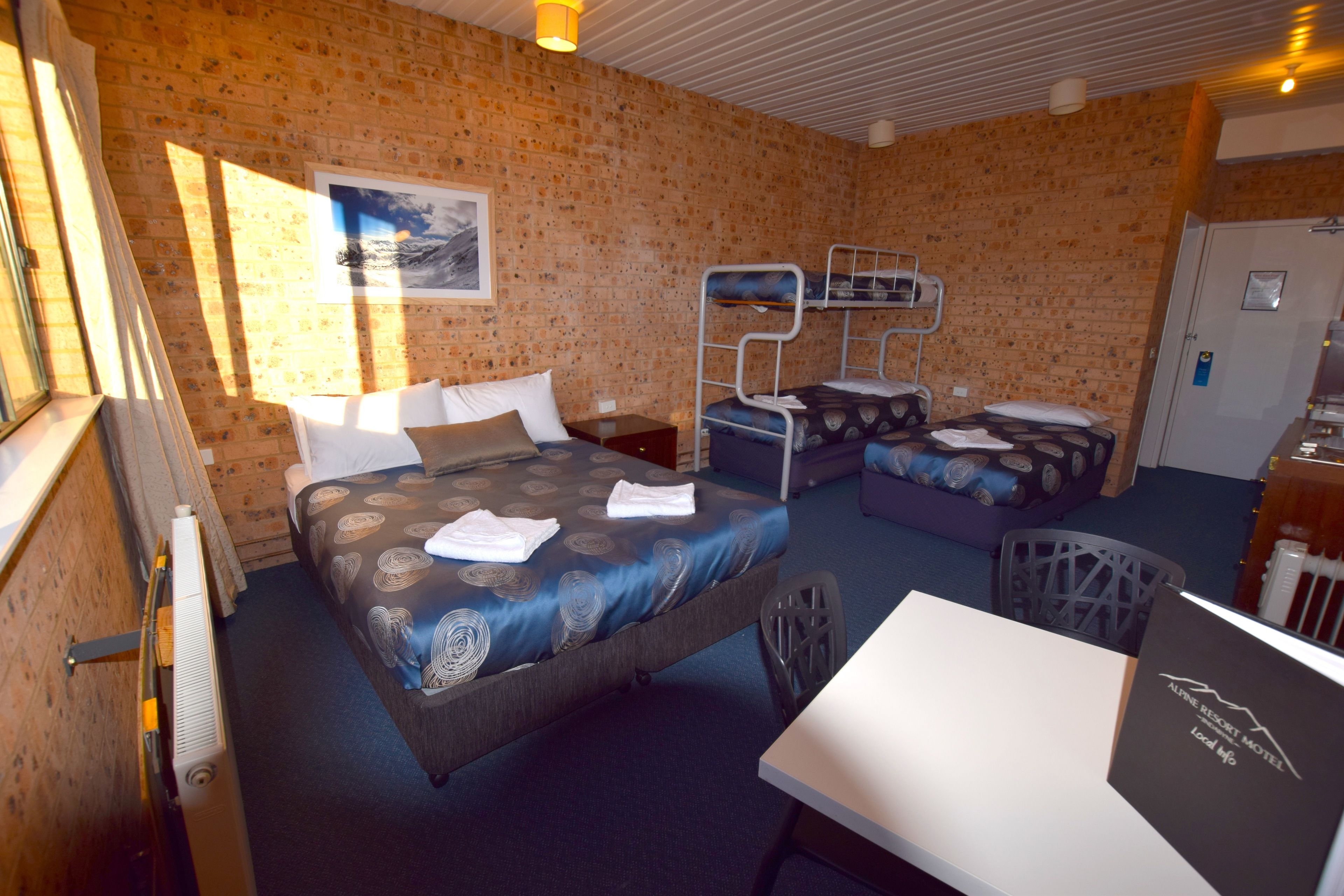 Une chambre d’hôtel avec un lit superposé, un bureau et une chaise. Il y a une fenêtre, un radiateur et une porte.