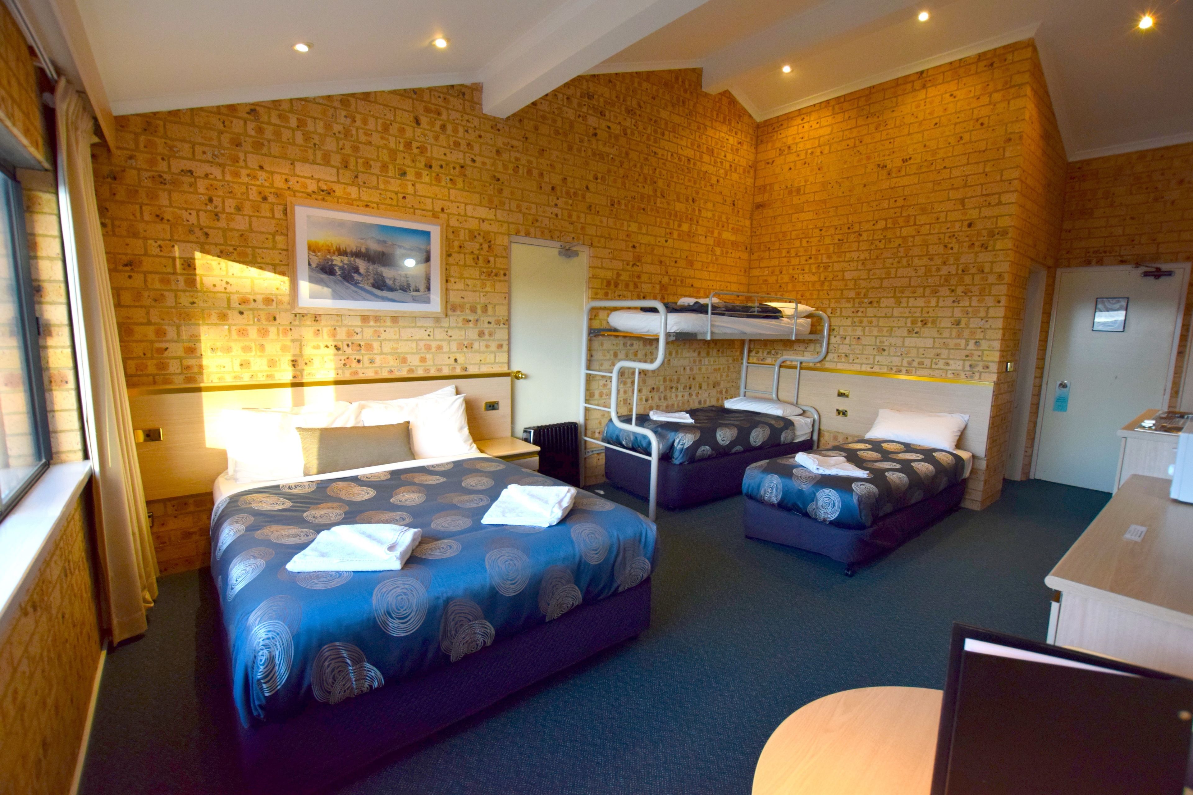 A hotel room with two beds, a desk, and a brick wall.