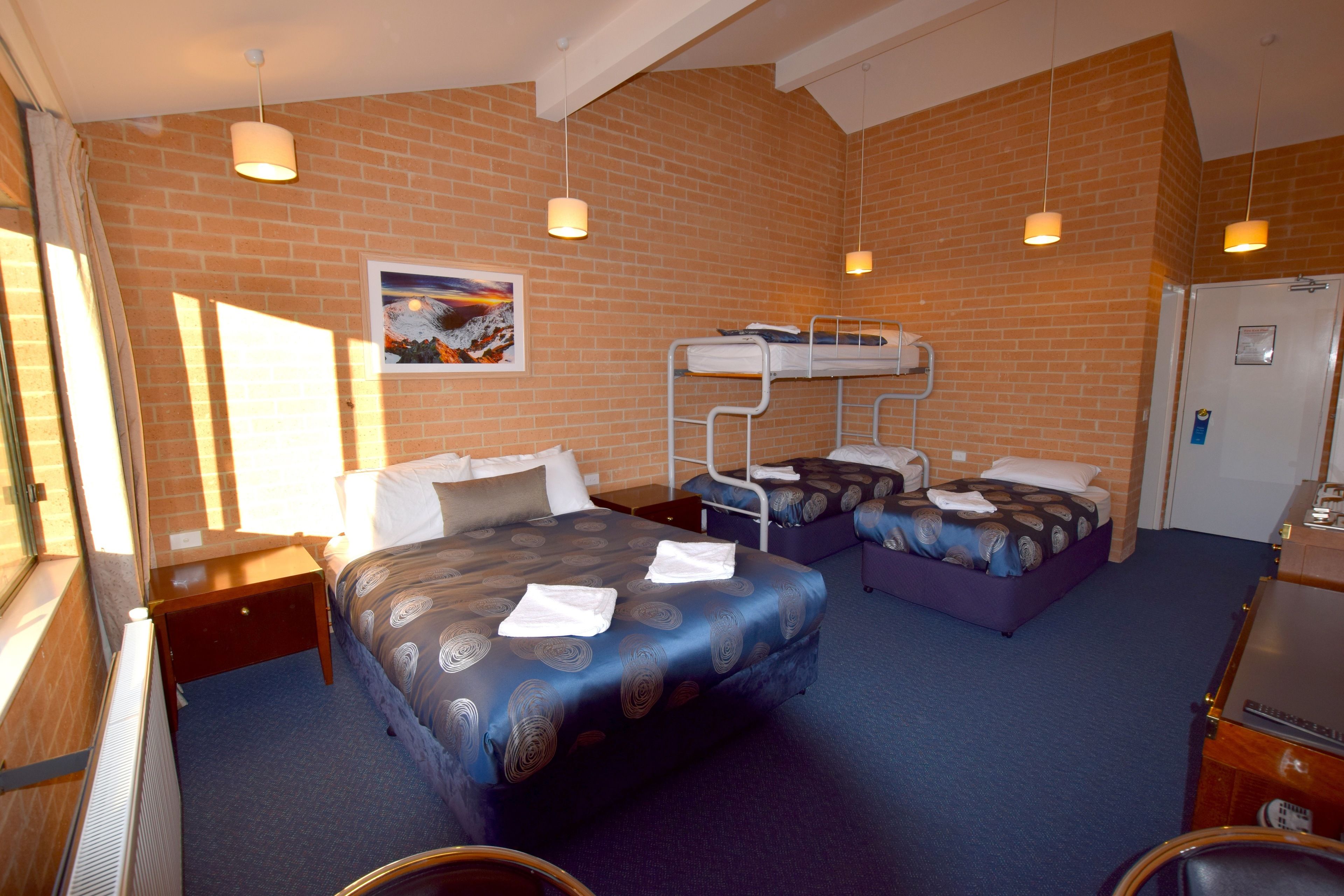 A hotel room with a bunk bed, a single bed, and a desk.
