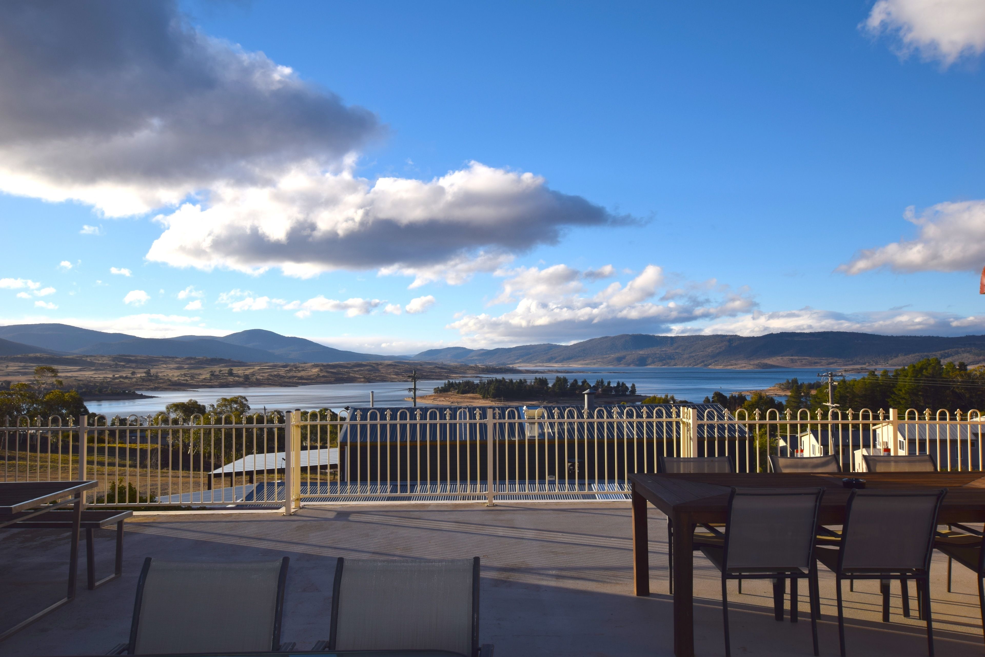 Een terras met een tafel en stoelen, met uitzicht op een meer en bergen.